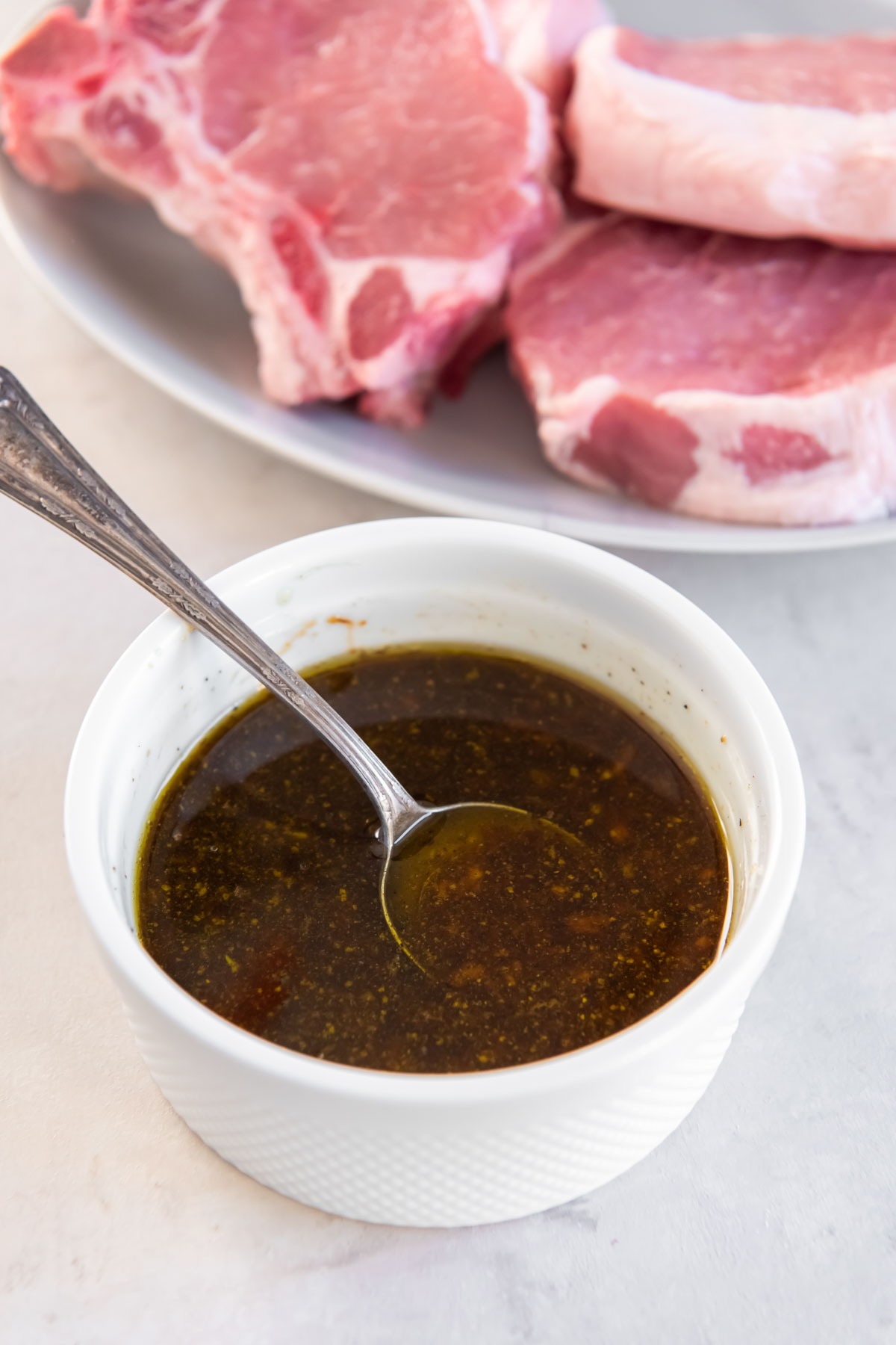 This delicious Pork Chop Marinade gives pork chops the best flavor! Easy to make with just 5 ingredients, use for grilled, baked or air fried chops. Pork chop marinade in small bowl with a spoon.